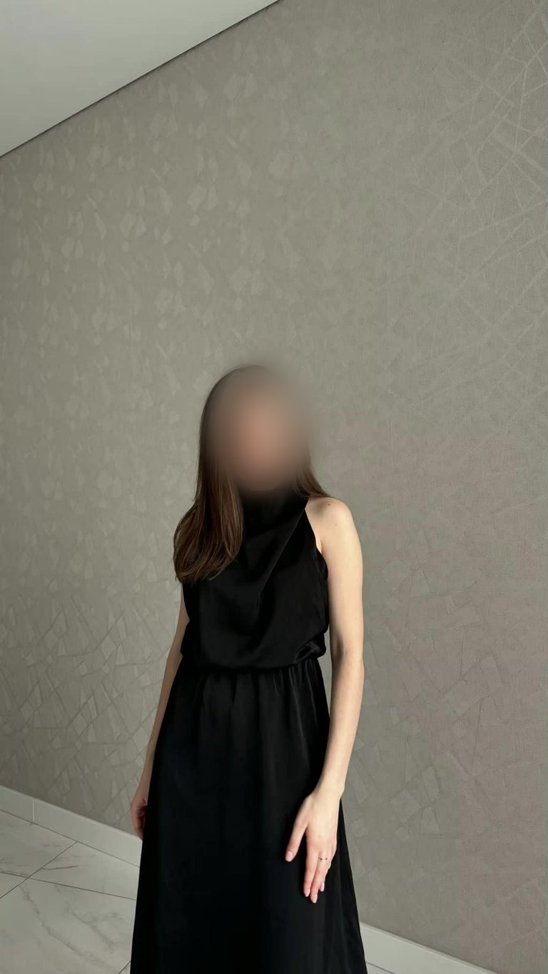 Elegant woman in black sleeveless dress posing indoors.