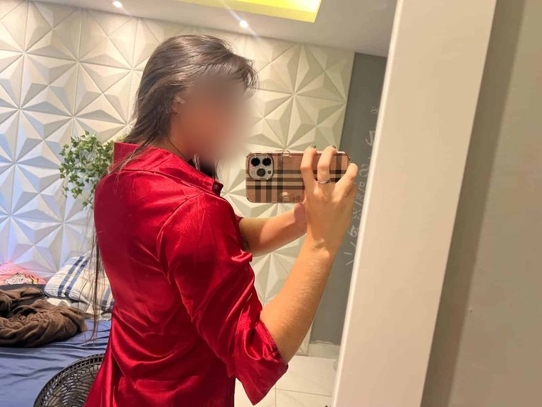 Woman in red satin shirt taking mirror selfie with phone.